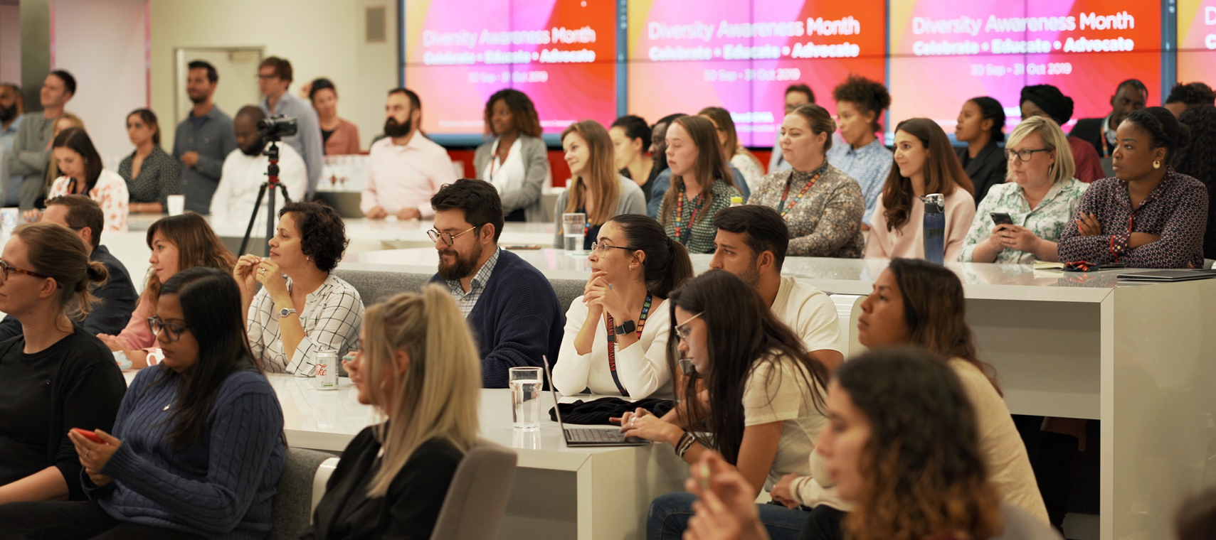 A diverse group of people attend a seminar for Diversity Awareness Month in a modern conference room.