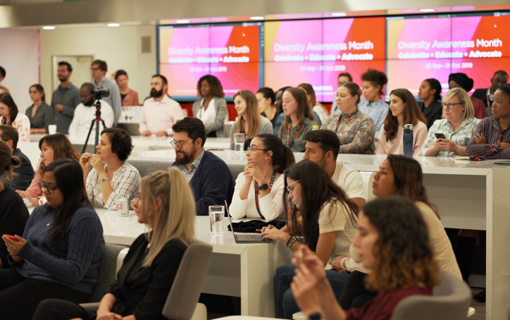 A diverse group of people attend a seminar for Diversity Awareness Month in a modern conference room.