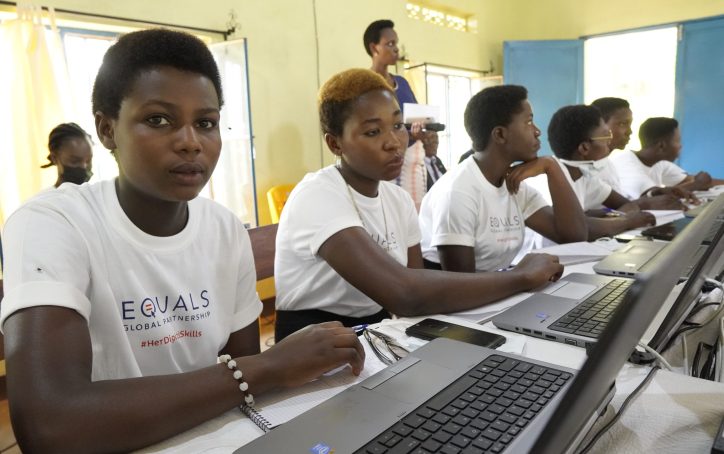 Young women sit at a table with laptops, participating in a tech workshop, wearing matching EQUALS shirts.