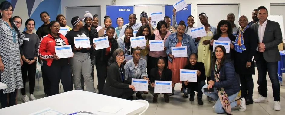 A large group of people pose indoors, holding certificates and smiling at the camera.