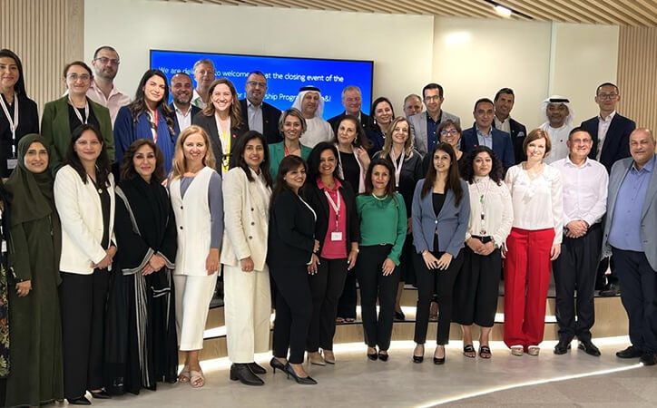 A diverse group of professionals pose together indoors, smiling for a group photo in business attire.