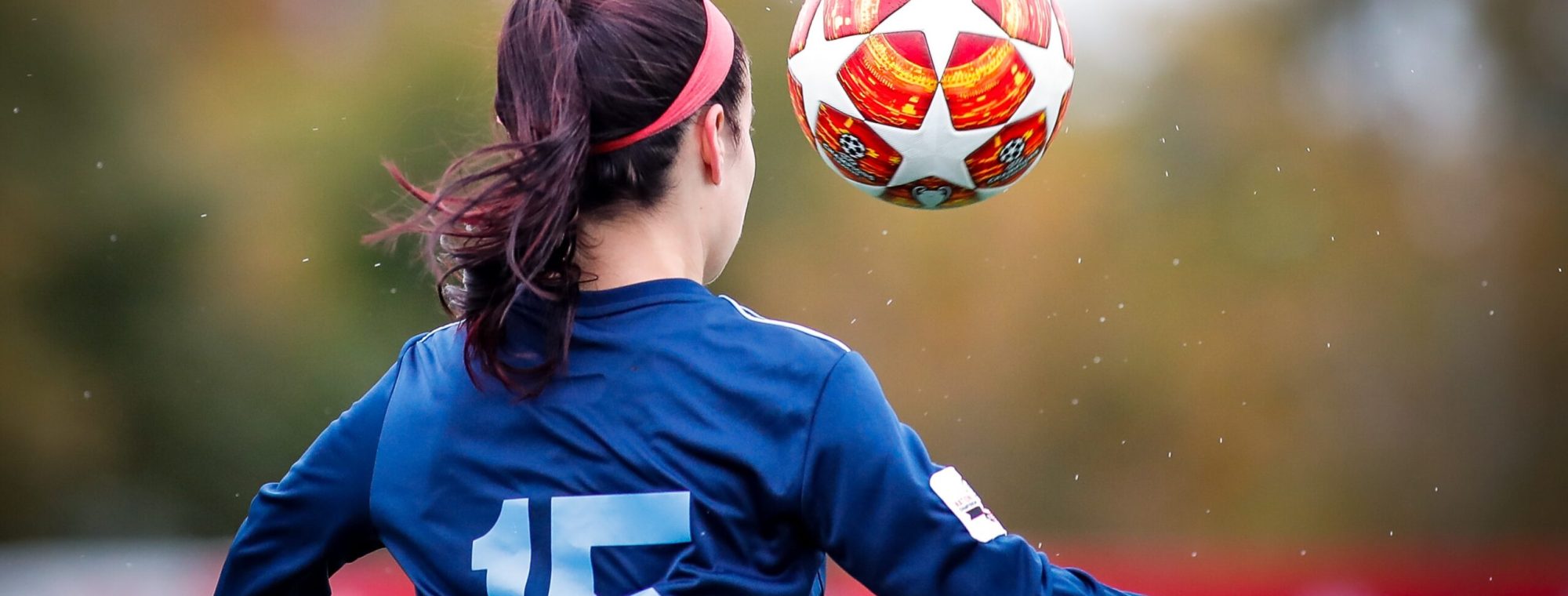 Soccer player in blue jersey #15 prepares to head a ball during a game, outdoors.