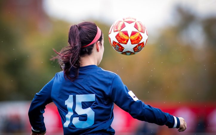 Soccer player in blue jersey #15 prepares to head a ball during a game, outdoors.
