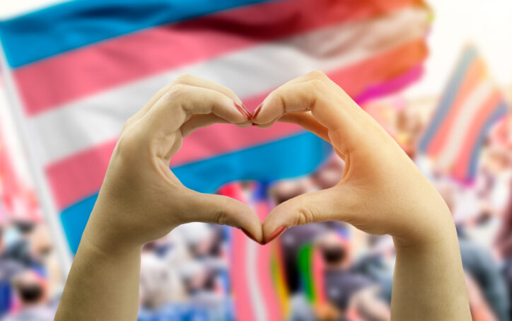 Two hands forming a heart in front of the transgender flag.
