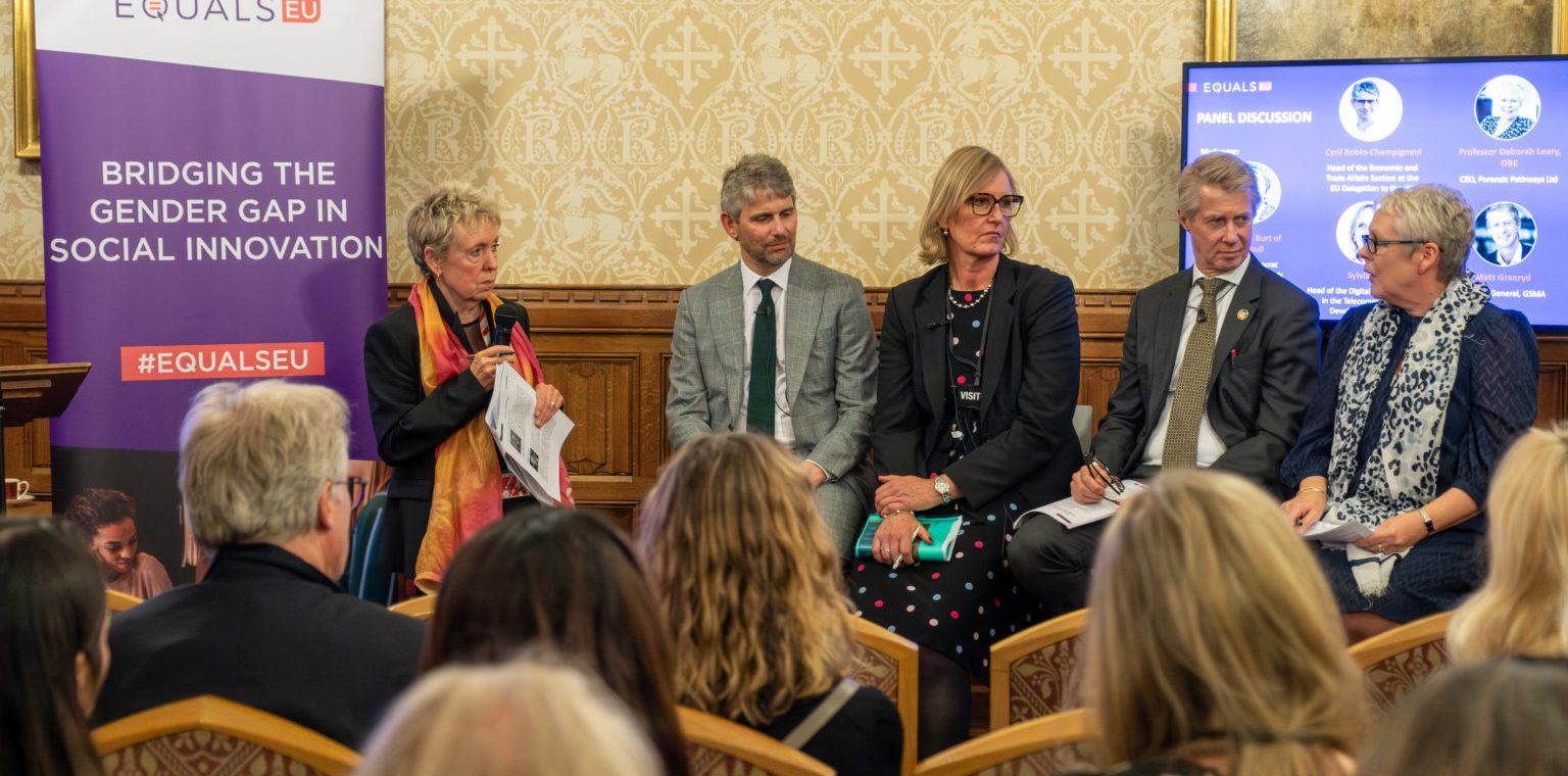 Five panelists discuss gender gap in social innovation at an event, with an audience seated in front of them.