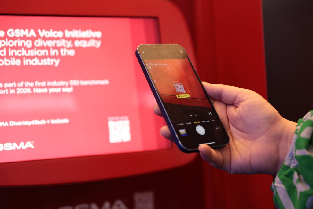 A person scans a QR code on a screen with their smartphone at an event.