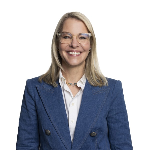 Smiling woman with blonde hair, wearing glasses, a blue blazer, and a white shirt, on a white background.