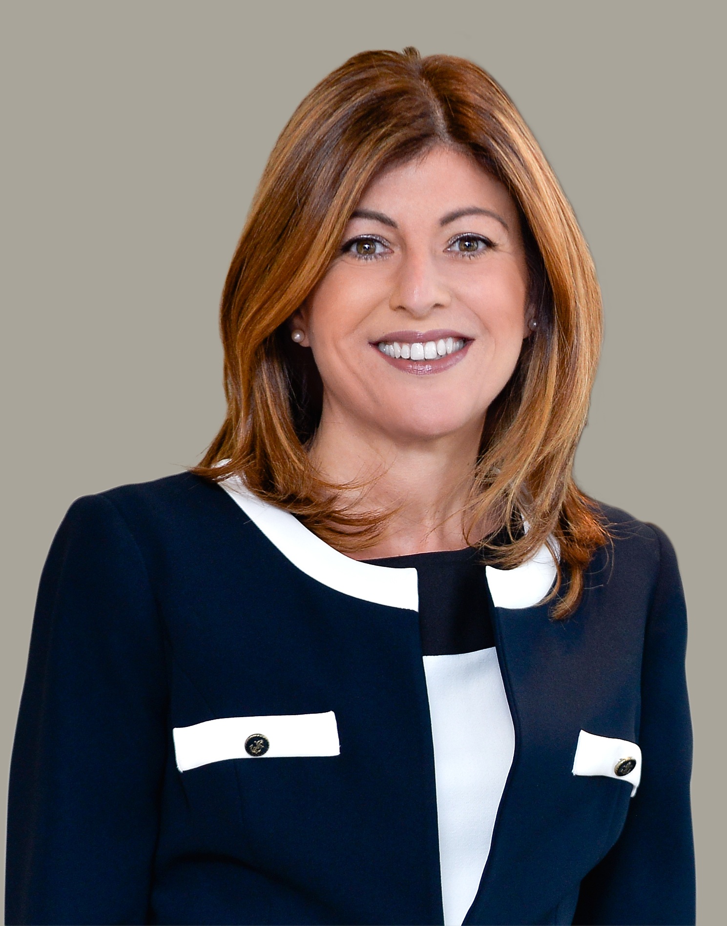 Smiling woman with straight brown hair wearing a black jacket with white trim, posed against a gray background.